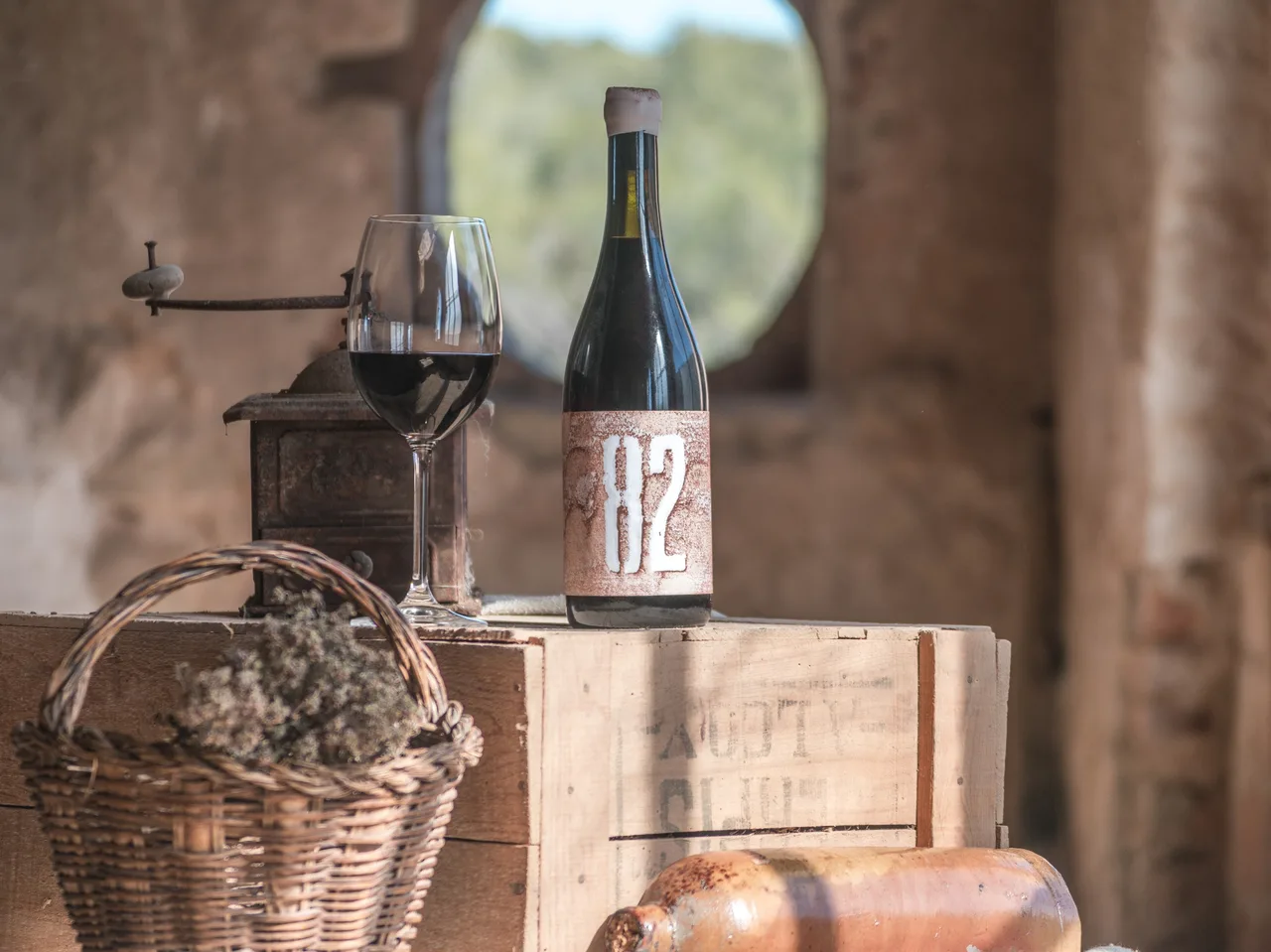Bottle of 82 red wine with a glass, a coffee grinder and a basket of thyme on a wooden crate