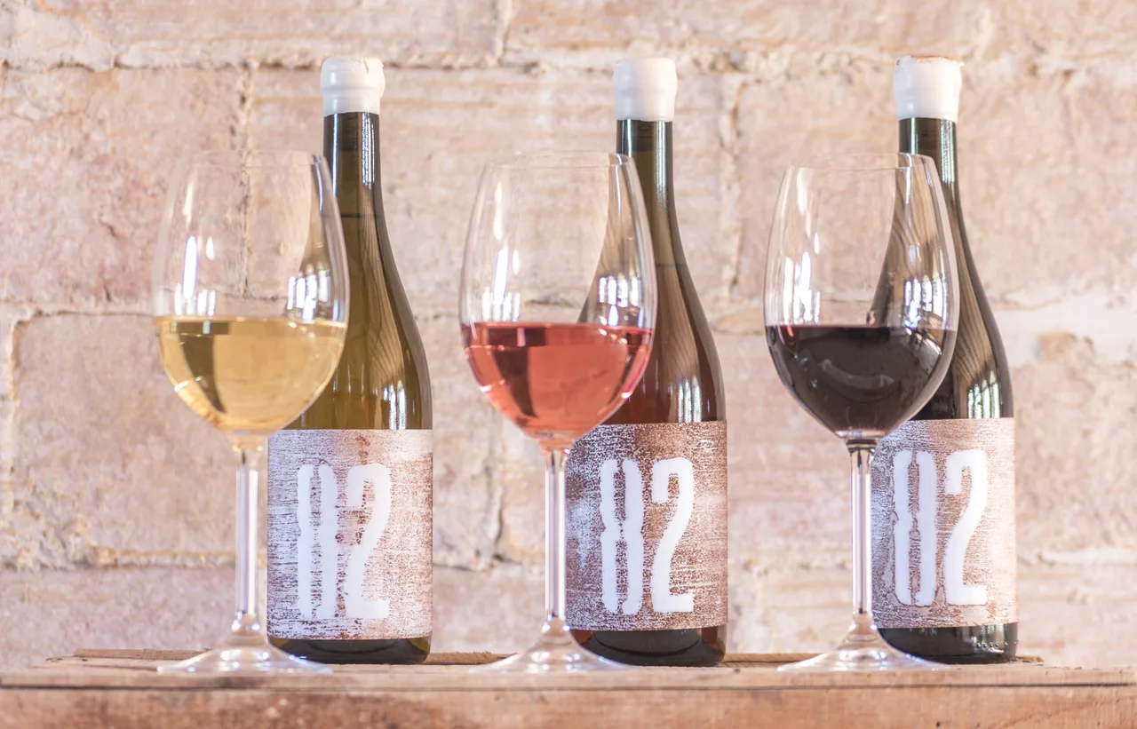 Three bottles of 82 white, rosé and red wine with glasses on a stone ledge, with the stamped label