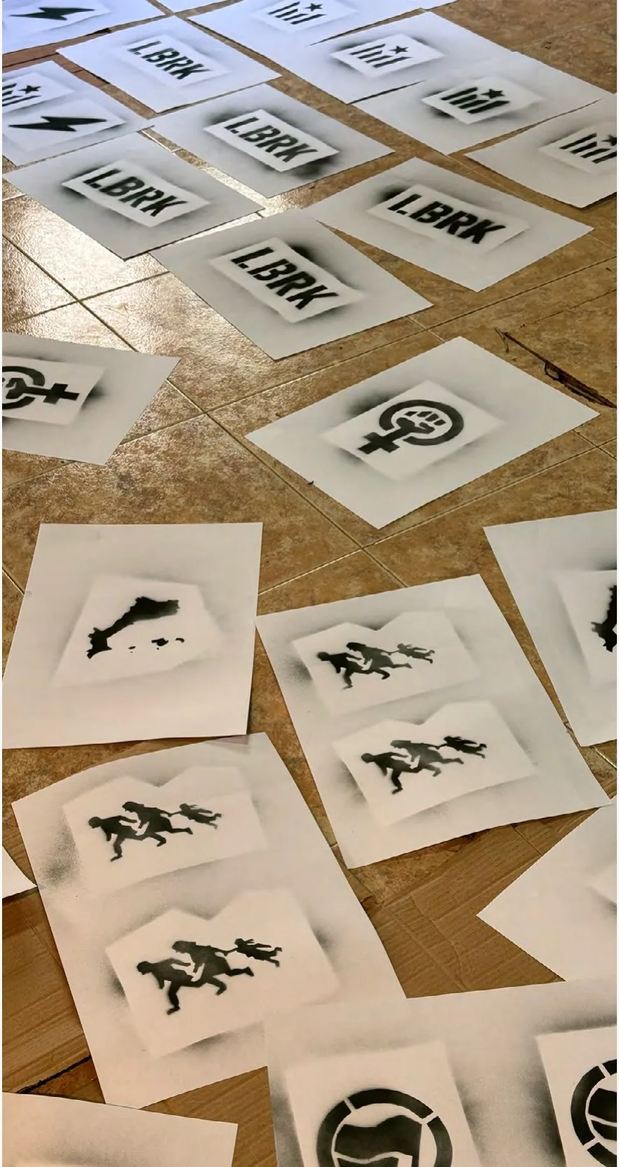 Impressions d'estencil sobre paper escampades per terra, amb figures i el text LBRK