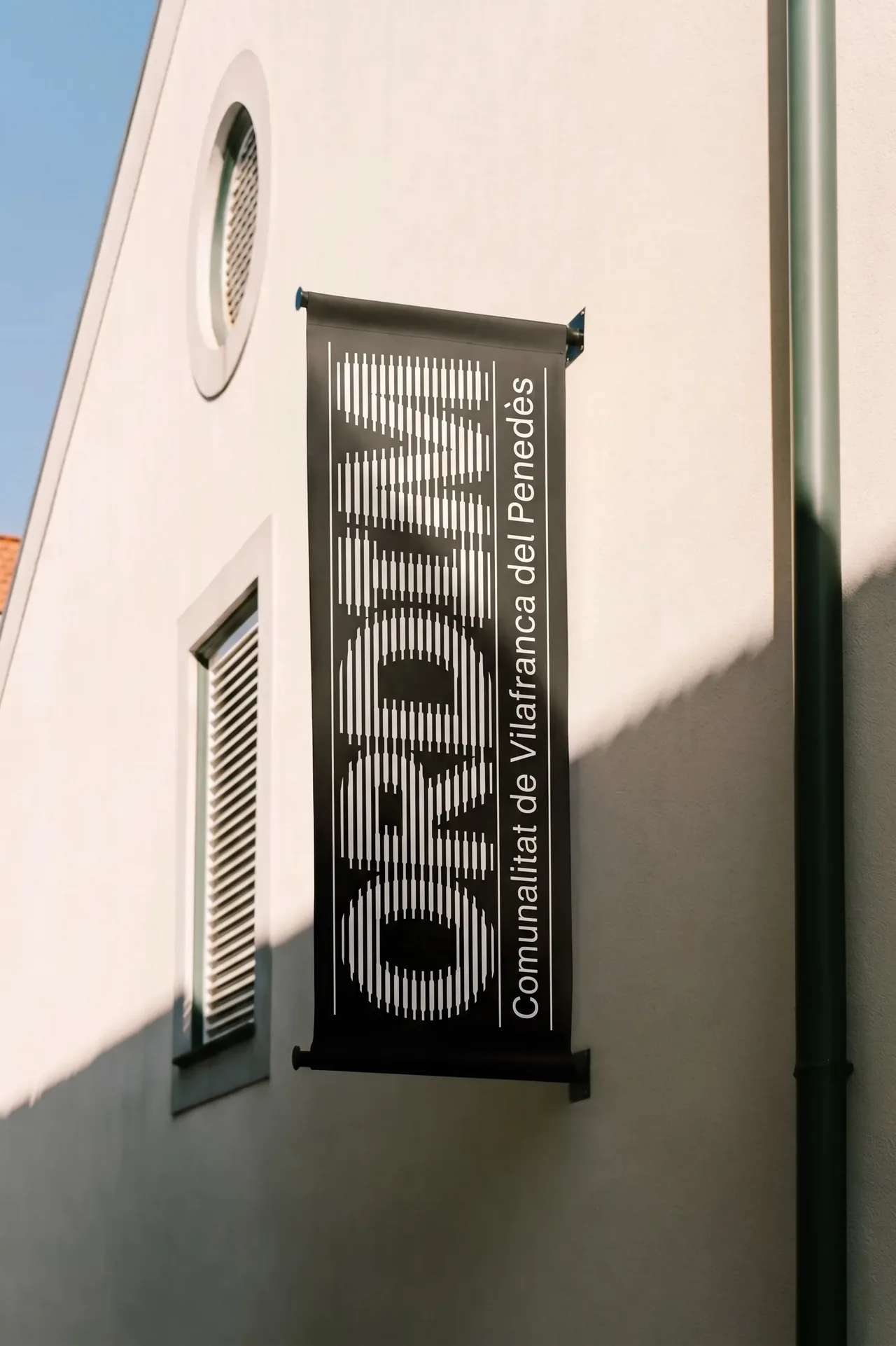 Bandera d'Ordim penjada a la façana d'un edifici, amb el logotip en negre