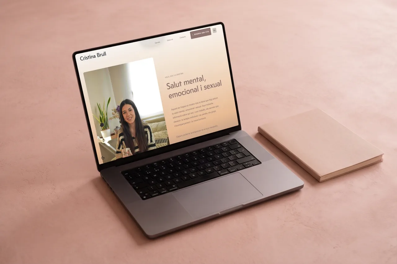 Laptop showing the home page of the website for a psychologist we built for Cristina Brull, on a soft pink surface